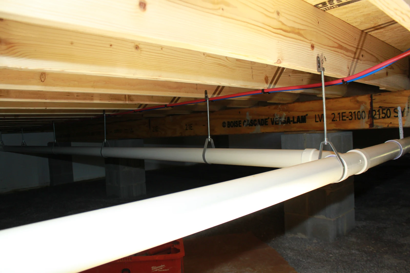 Supported drain piping and red and blue water lines beneath the floor